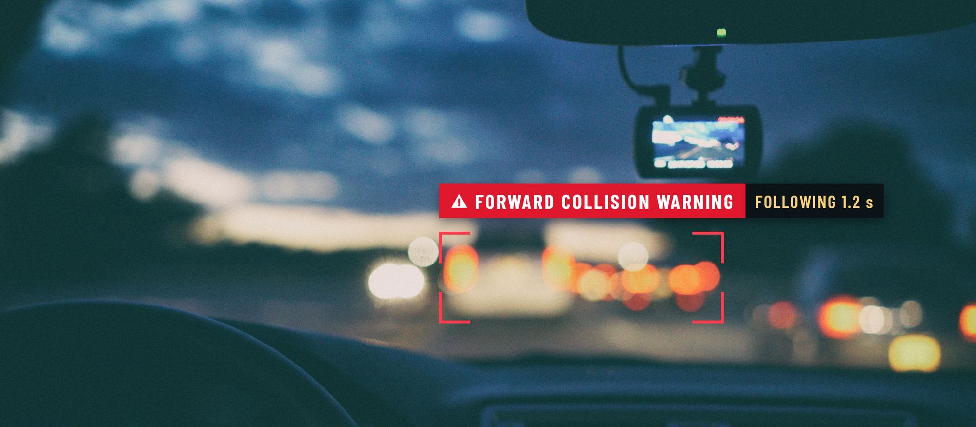 View through a windshield at dusk with a dash cam mounted by the mirror and brake lights ahead, marked with a forward collision warning alert