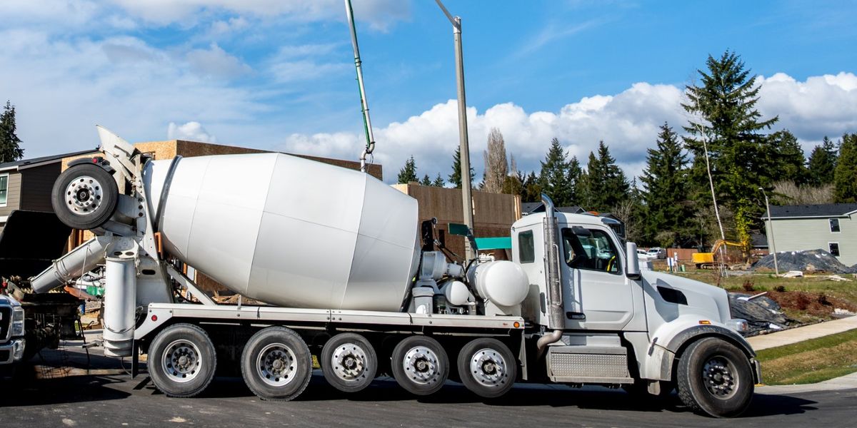 A white five-axle concrete mixer truck feeds a boom pump at a new housing development