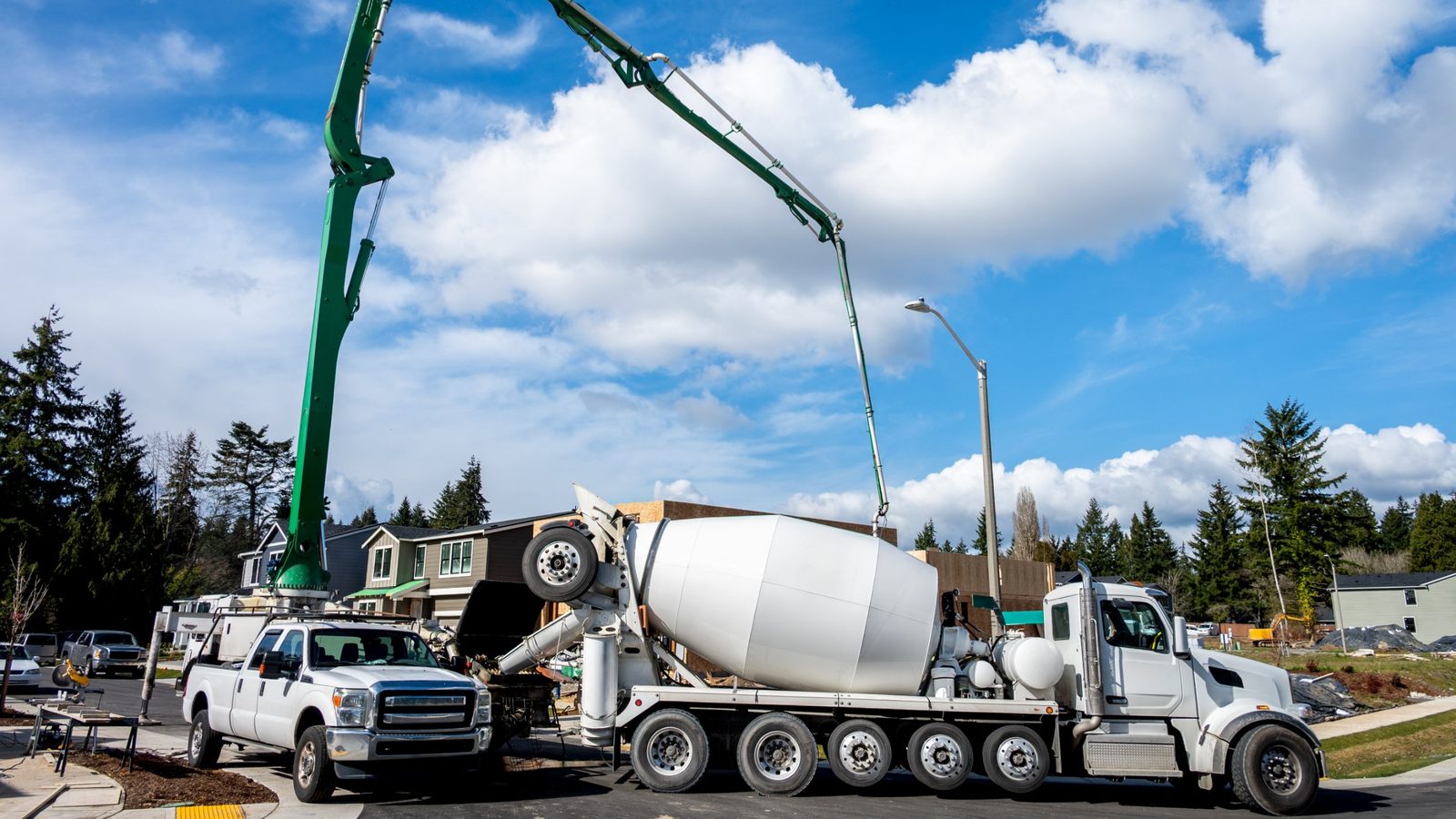 A white five-axle concrete mixer truck feeds a boom pump at a new housing development