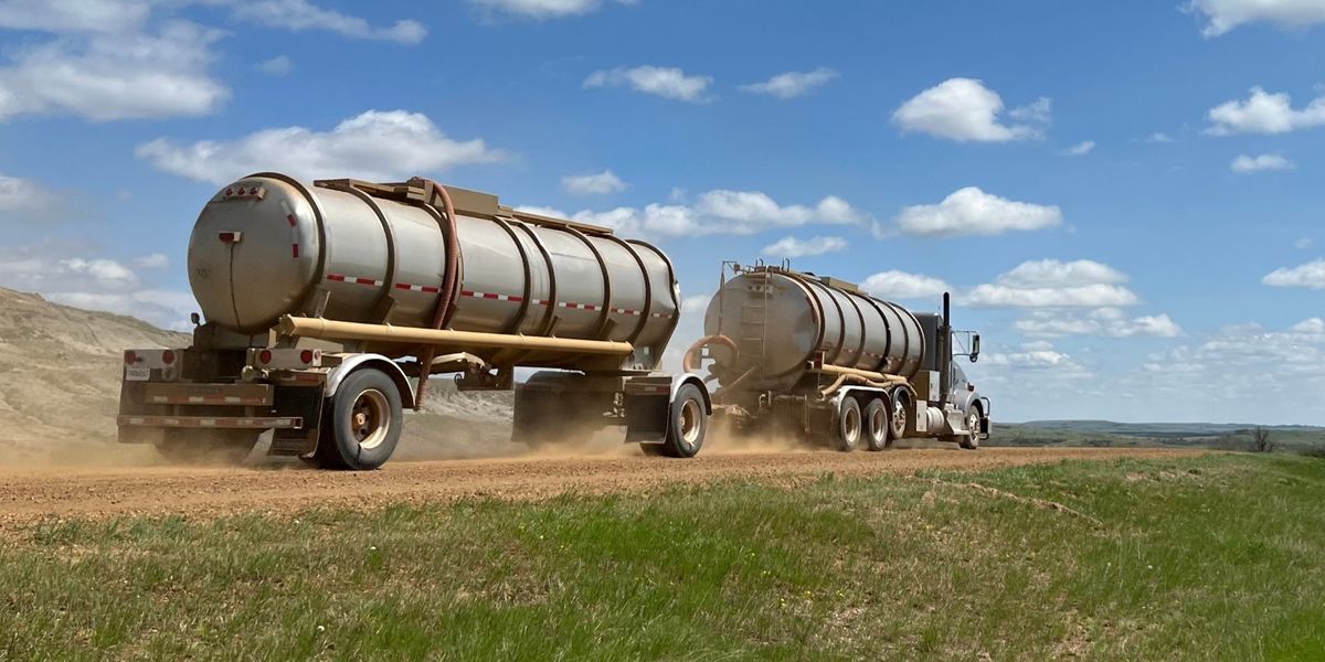 A crude oil tanker truck pulling a second tank trailer kicks up dust on a gravel lease road across the North Dakota prairie