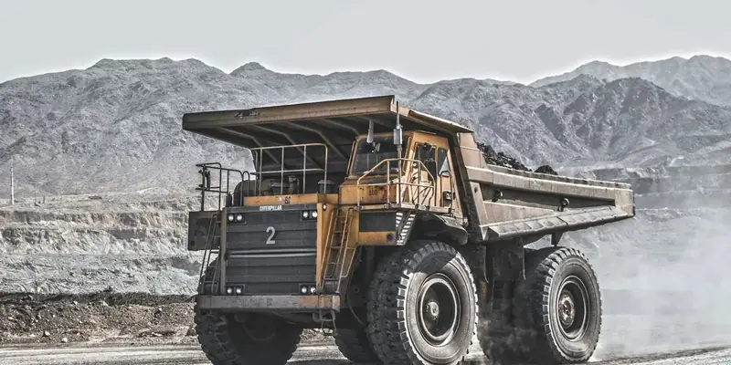 A large mining haul truck drives a dusty haul road below rocky mountains