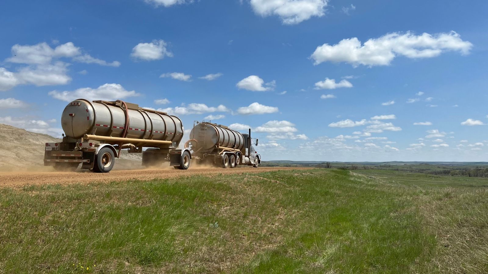 A crude oil tanker truck pulling a second tank trailer kicks up dust on a gravel lease road across the North Dakota prairie
