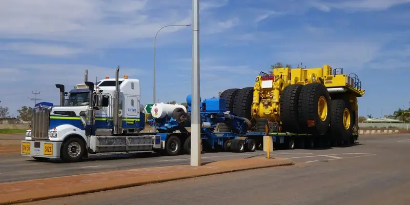 A semi tractor pulls a multi-axle lowboy carrying an oversize yellow mining truck