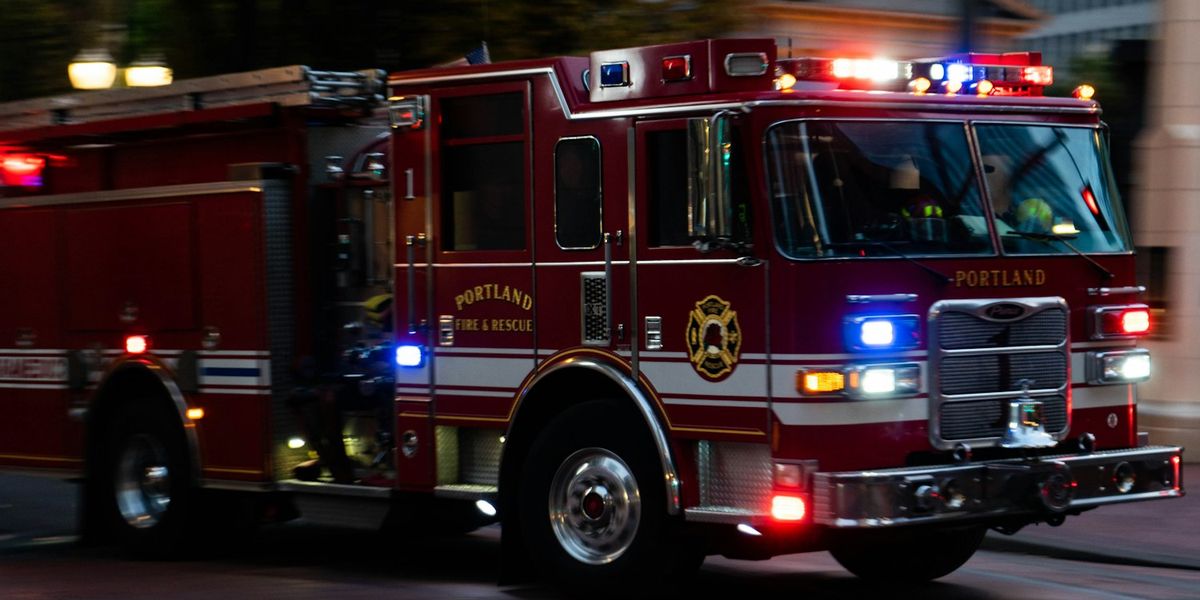 A Portland Fire & Rescue engine runs with red and blue lights flashing on a city street at dusk
