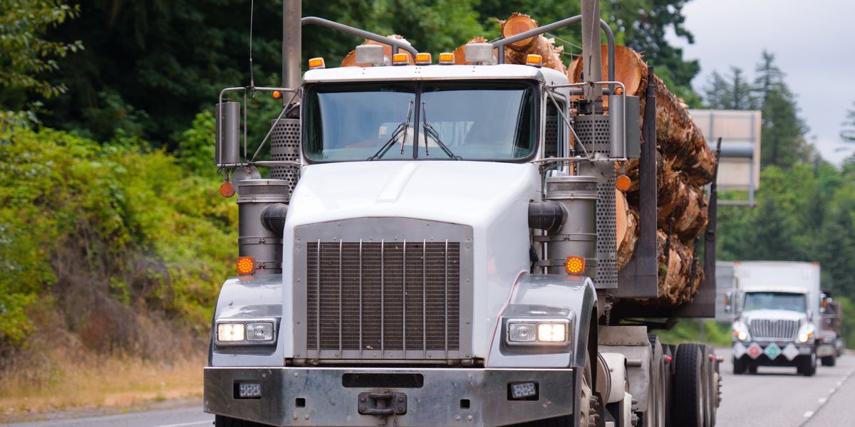 A long-hood log truck hauls a full load of logs down a forested highway in the Pacific Northwest