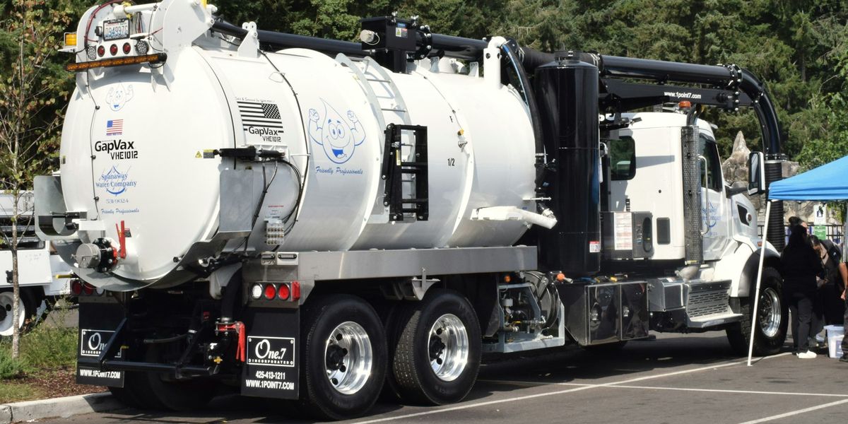 A white tandem-axle vacuum truck with a large debris tank and boom parked in a lot in Washington State