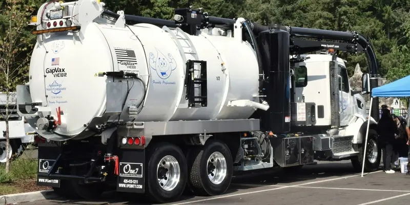 A white tandem-axle vacuum truck with a large debris tank and boom parked in a lot in Washington State