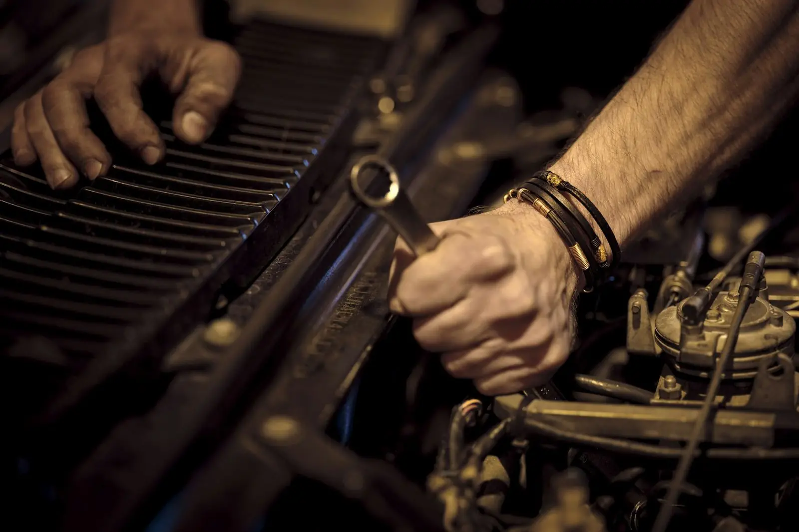 A mechanic’s greasy hands work on a truck engine with a wrench
